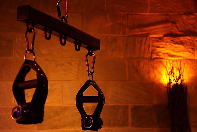 Dungeon-Eyes Wide Shut leather restraints hanging in a dimly lit room for overnight fetish experience London