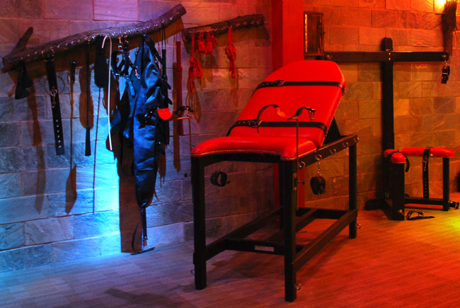 Interior view of private dungeon rental London with red padded bondage furniture and wall restraints