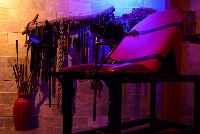 Room setup with bondage equipment and a red padded bench for private dungeon rental London experience